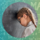 A young girl with glasses leans her head against a blackboard filled with Maths equations, symbolising anxiety and frustration towards learning Maths